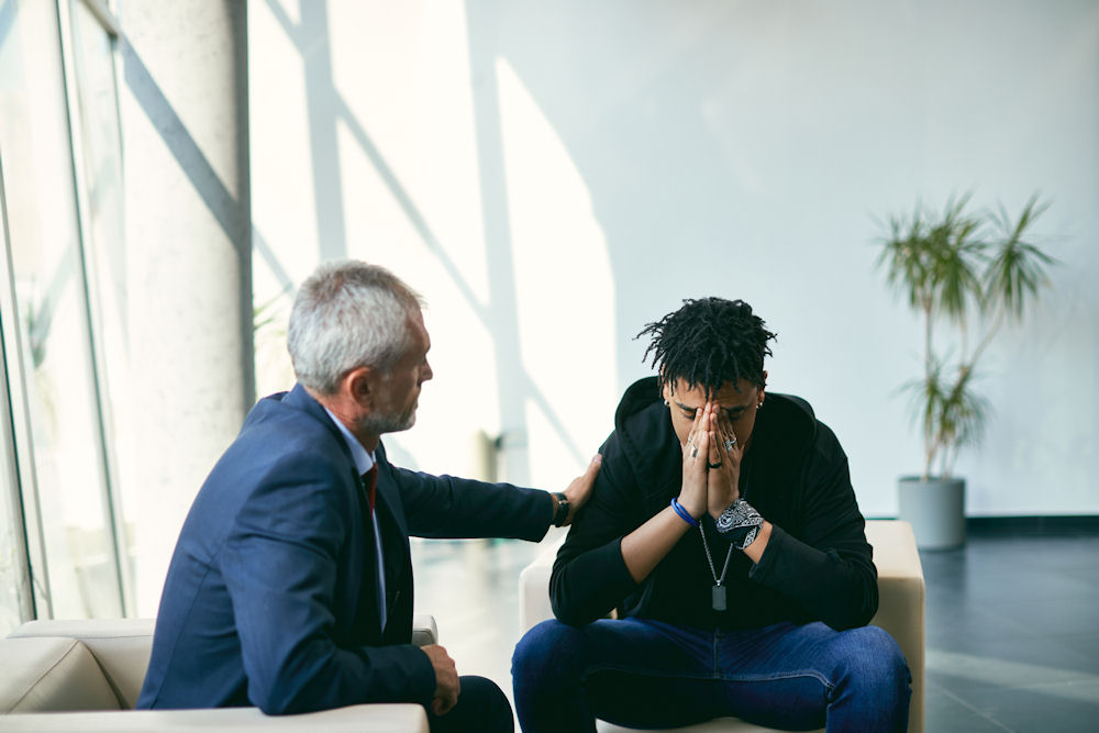 Unhappy African American teenager on meeting with his therapist at psychotherapy center.